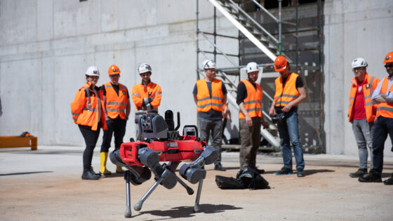 Metal industry workers observing an autonomous inspection robot at a steel plant site.